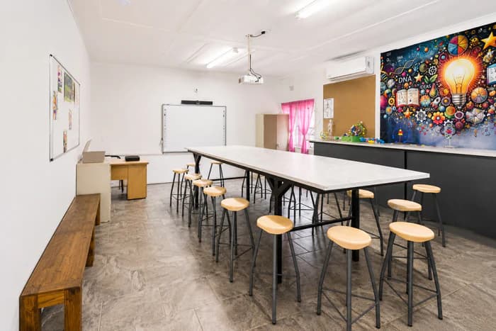 A bright Da Silva Academy learning space with a central worktable, stools and an educational mural.