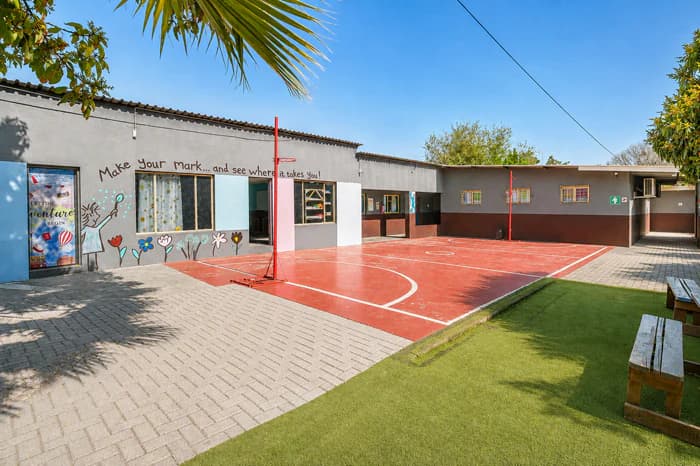 A clean outdoor activity court at Da Silva Academy, bordered by school buildings, trees and landscaped grounds.